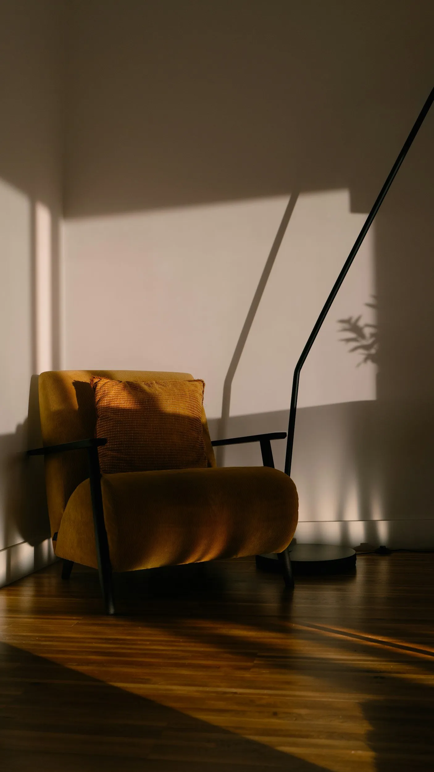 A mustard armchair in the corner of a quiet room, lit by low evening sun through a window
